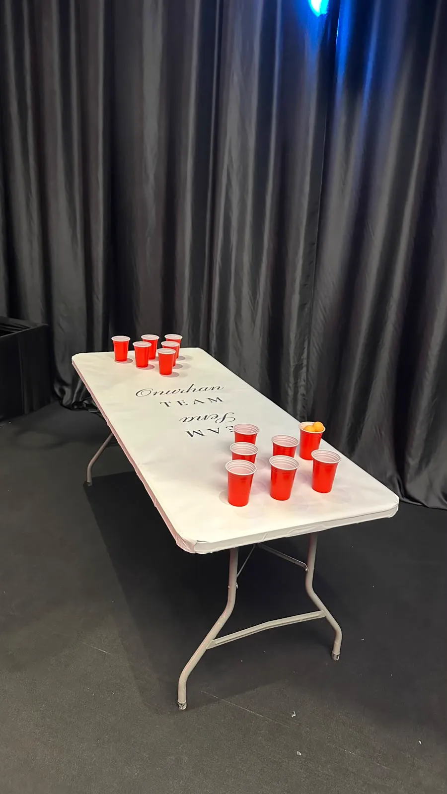 Takım isimleri yazılı beyaz beer pong masası ve kırmızı bardaklar